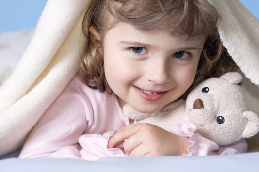 Kind mit Kuscheltier unter einer Decke